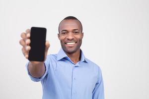 It is for you. Cheerful black man stretching out a mobile phone and smiling while standing isolated on grey photo