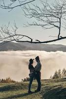 encontraron el amor. toda la longitud de una pareja joven parada cara a cara mientras disfruta de la vista perfecta de la cordillera foto