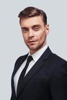 Always in style. Handsome young man in full suit looking at camera with smile while standing against grey background photo