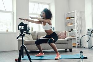 Beautiful young African woman crouching using strap while making social media video photo