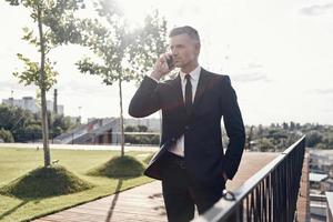 Confident mature businessman talking on mobile phone while walking outdoors