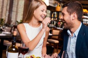 Try my meal Beautiful young loving couple enjoying dinner at the restaurant while woman feeding her boyfriend with salad photo