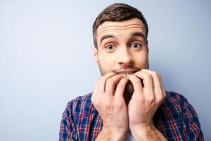 Terrified with something. Frustrated young man in casual shirt keeping mouth open and looking terrified while standing against grey background photo