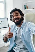Playful young African man smiling and looking at camera while taking selfie indoors photo