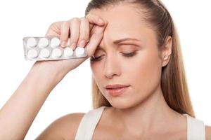 Woman with medicines. Depressed young woman holding medicines and touching head with hand while standing isolated on white photo