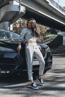 Beauty in style. Full length of attractive young woman posing while leaning on the car outdoors photo