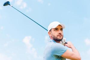 golfista confiado. vista de ángulo bajo de un joven serio jugando al golf mientras está de pie al aire libre foto