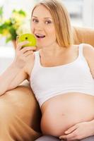 alimentación fresca y saludable. hermosa mujer embarazada sentada en la silla y comiendo manzana verde foto