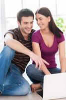 Surfing the net together. Beautiful young couple working on laptop together while man pointing monitor and smiling photo