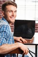 Surfing the net is fun. Rear view of handsome young man looking over shoulder and smiling while sitting at his working place photo