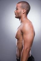 He got perfect body. Side view of young shirtless African man standing against grey background photo