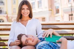 We love spending time together. Beautiful young loving couple bonding to each other while sitting together on the bench photo