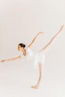 Skill and grace. Full length side view of beautiful young ballerina in white tutu dancing against white background photo