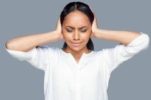 sentirse cansado y estresado. joven africana frustrada cubriendo los oídos con las manos y manteniendo los ojos cerrados mientras se enfrenta a un fondo gris foto