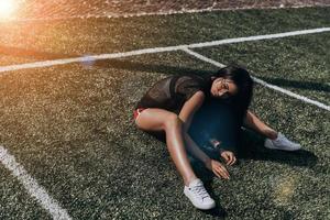 mujer delgada y atractiva. bella joven con ropa deportiva mirando a la cámara mientras se sienta en el campo de fútbol foto