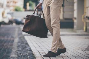 Perfect match. Close-up of man holding leather bag while walking outdoors photo