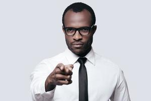 Time for you to make decision. Portrait of handsome African man in eyeglasses pointing you while standing against grey background photo