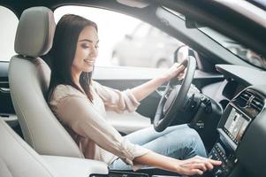 Searching for favorite music. Young attractive woman smiling and pushing buttons while driving a car photo