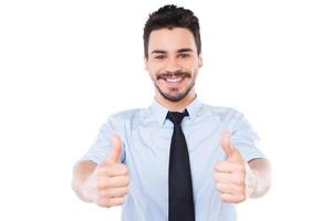 I say yes Confident young man in shirt and tie looking at camera and showing his thumbs up and smiling while standing against white background photo