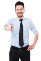 I choose you Handsome young man in shirt and tie pointing you and smiling while standing against white background photo