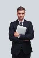 Young and successful. Handsome young man carrying digital tablet and looking at camera with smile while standing against grey background photo