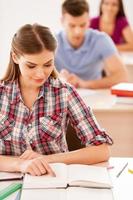 Student reading a book. Top view of beautiful female student reading a book while sitting in classroom with other students sitting in a row behind her photo