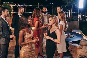 Group of beautiful young people in formalwear communicating and smiling while spending time on luxury party photo