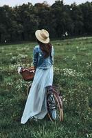 New adventures are coming. Full length rear view of young woman wearing dress and hat while standing with her old fashioned bicycle photo