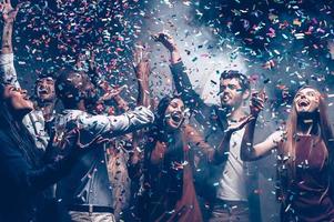 Multi colored fun. Group of beautiful young people throwing colorful confetti while dancing and looking happy photo