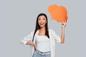 Beautiful young Asian woman looking at camera and smiling while standing against grey background photo