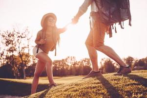 Always ready to help. Man with backpack helping woman to climb the hill while holding her hand photo