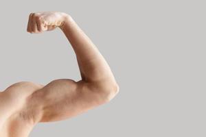 Perfect shape. Cropped image of muscular man showing his perfect biceps while isolated on grey background photo