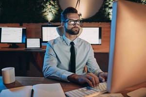 Confident young man working on computer while staying late in the office photo