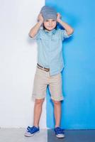 Life in colors. Full length of handsome little boy adjusting his hat and looking at camera while standing against colorful background photo