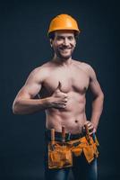 Attractive construction worker. Young confident man gesturing and looking at camera while standing against black background photo