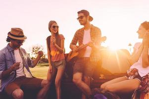 Enjoying road trip with friends. Group of young cheerful people dancing and playing guitar while enjoying their road trip in pick-up truck together photo