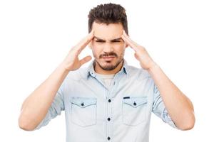 Too much stress. Frustrated young man touching head with fingers and looking at camera while standing against white background photo