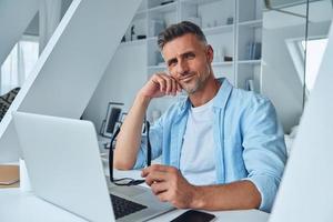 Confident mature man looking at camera while sitting at the office desk photo