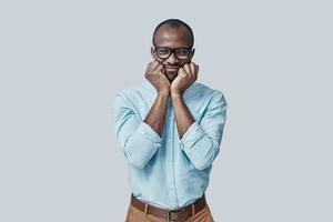 Happy young African man looking at camera and smiling while standing against grey background photo