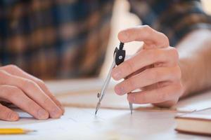 It is all about accuracy. Close-up of young man using compass for drawing photo