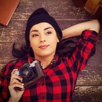 Creative photographer. Top view of beautiful young woman in headwear lying on the floor and holding camera while suitcase and note pad laying near her photo