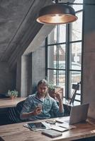 Another business message. Serious young man holding a mobile phone and looking at it while sitting at office desk near the window photo