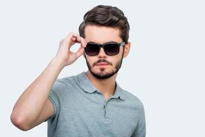 Confident in himself. Confident young man adjusting eyewear and looking at camera while standing against white background photo