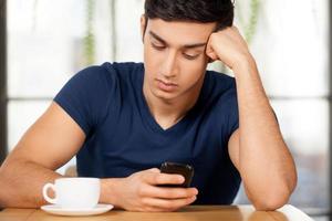 sentirse solo sin ella. joven frustrado sentado en el restaurante y mirando su teléfono móvil foto