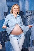 mezclilla de embarazo. hermosa mujer embarazada con ropa de jeans posando mientras está de pie contra el fondo de los jeans foto