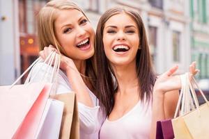 nos encanta ir de compras juntos. dos mujeres jóvenes felices sosteniendo bolsas de compras y sonriendo mientras están de pie al aire libre foto