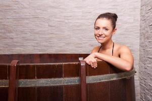 Beauty treatment. Beautiful young woman sitting in a barrel with water and smiling photo