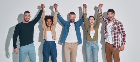 grupo de jóvenes hermosos con ropa informal tomándose de la mano y sonriendo foto