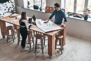 Full concentration. Top view of young colleagues in smart casual wear using blueprint while working in the creative working space photo