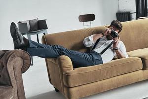 Handsome young man photographing using his camera while lying on sofa photo